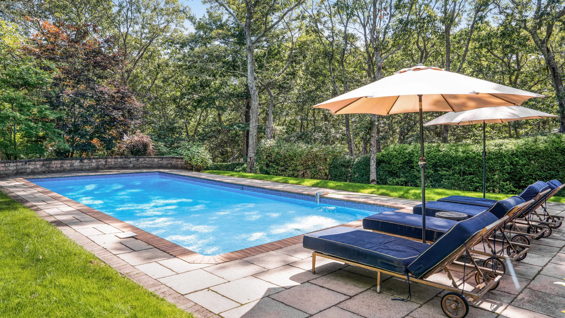 Una piscina al aire libre junto a asientos y sombrillas, rodeada de árboles.