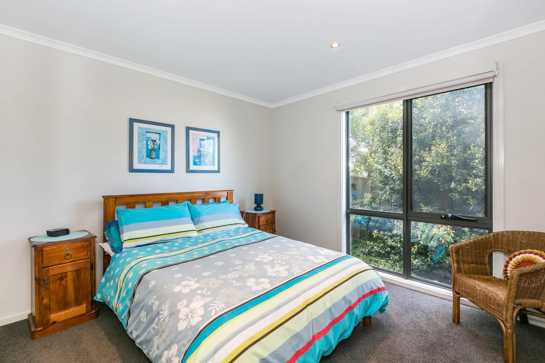 Un dormitorio con una cama bien hecha y una ventana amplia con vista a árboles frondosos.