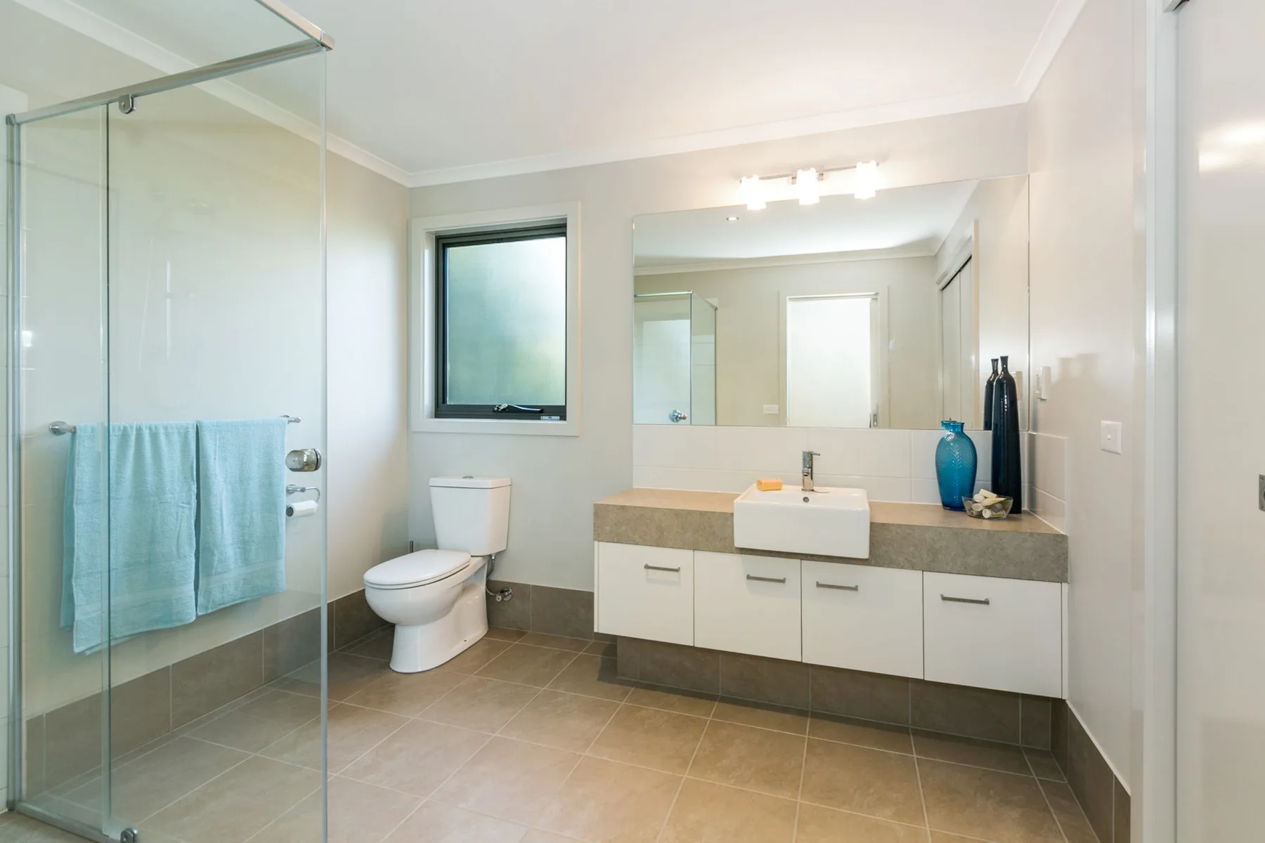 Un baño luminoso con ducha de vidrio, inodoro y lavabo.
