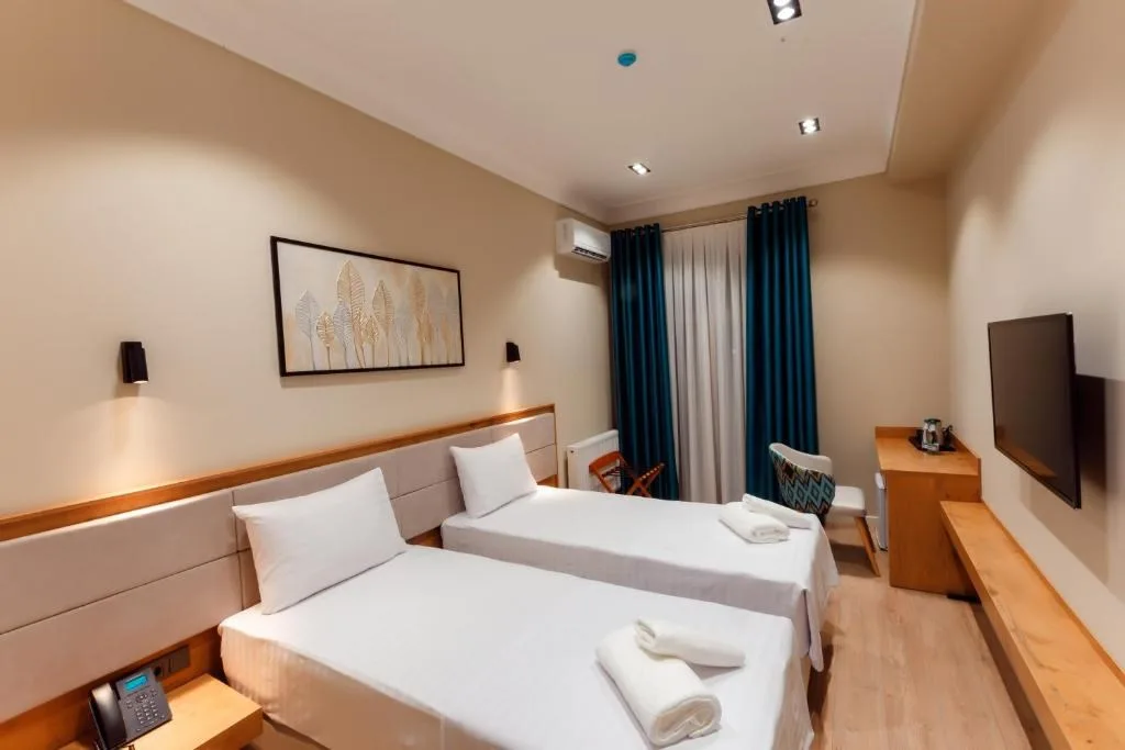 Espacio representativo del hotel: Un dormitorio de hotel con dos camas y cortinas verde azulado.