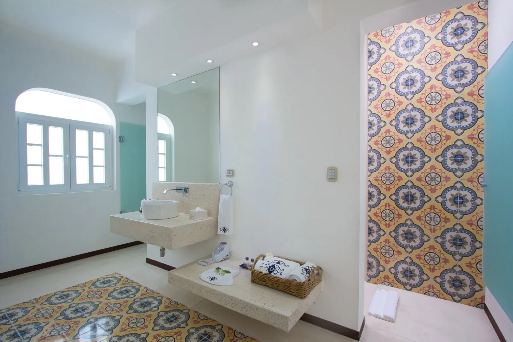 Espacio representativo del hotel: Un baño luminoso tiene un lavabo, suelo estampado y una pared de ducha con azulejos coloridos.