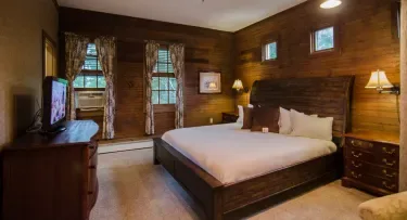 Representative hotel space: A bedroom with a large bed, wooden walls, and curtained windows.