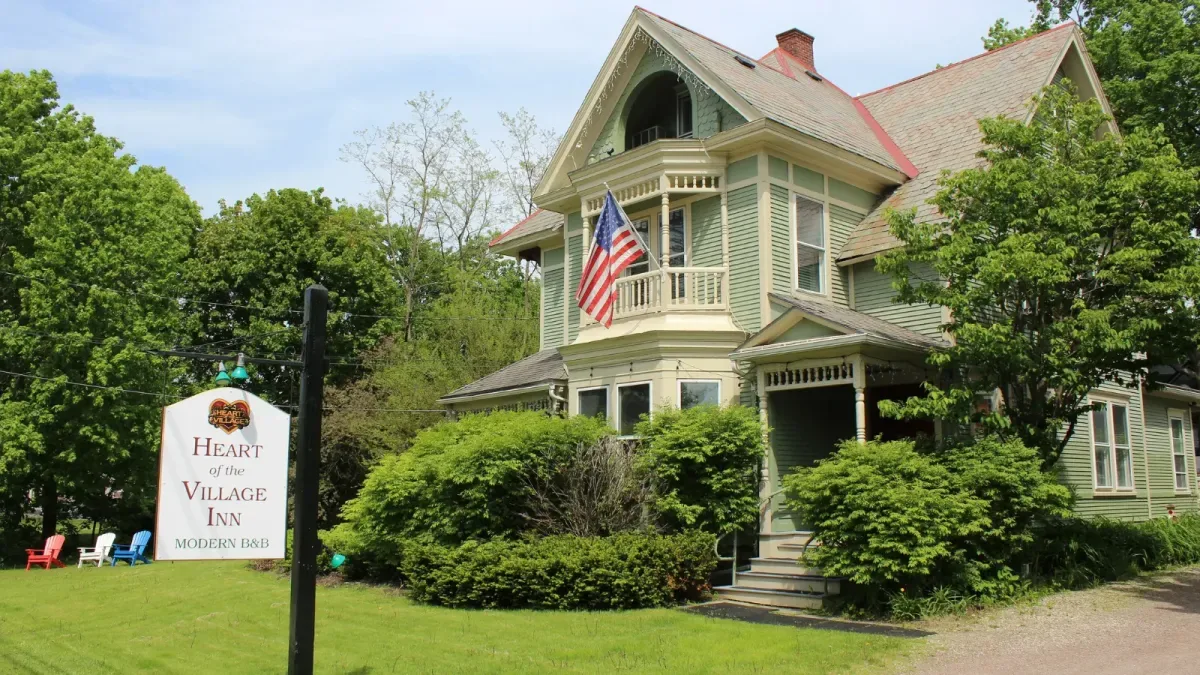 Representative hotel space: A large green house with a front porch stands beside a lawn and trees.