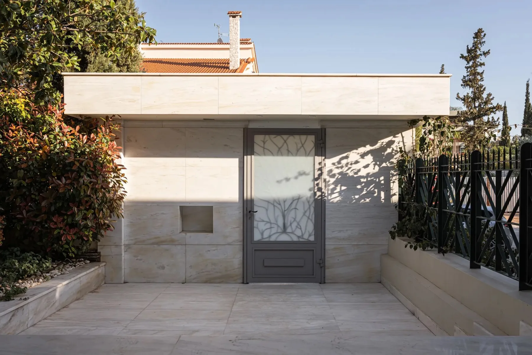 A paved outdoor entrance with a central door, flanked by plants and a railing.