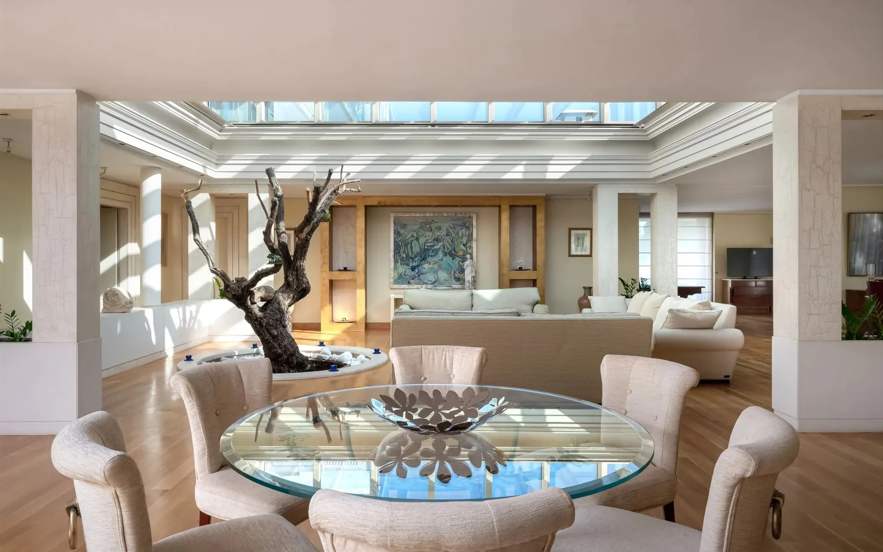 A bright living room with an oval glass table and seating beneath a skylight.