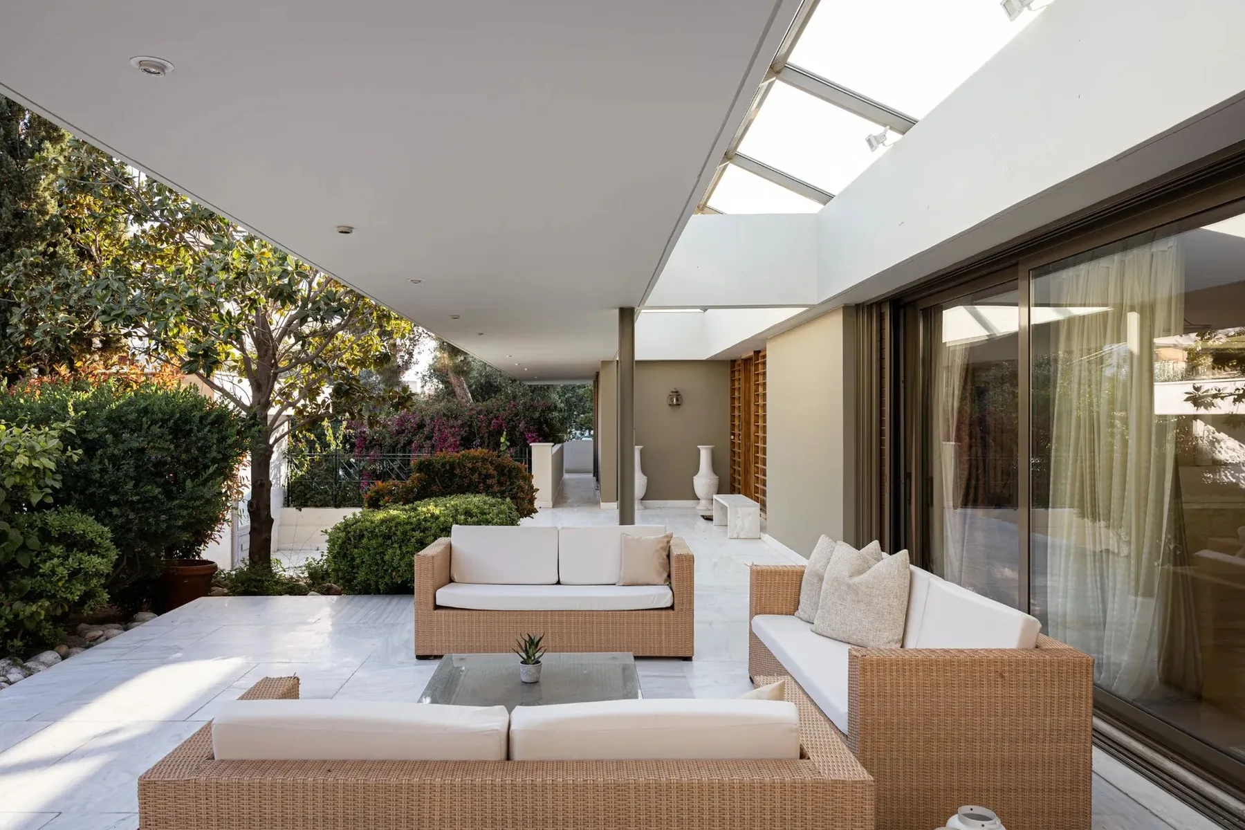 A bright outdoor patio with cushioned seating beside glass doors and garden greenery.