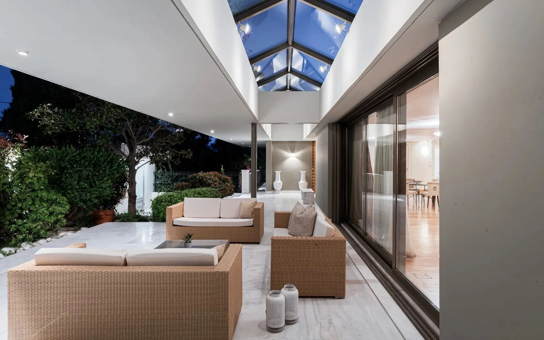 A covered outdoor seating area beside large glass doors, with a skylight overhead.