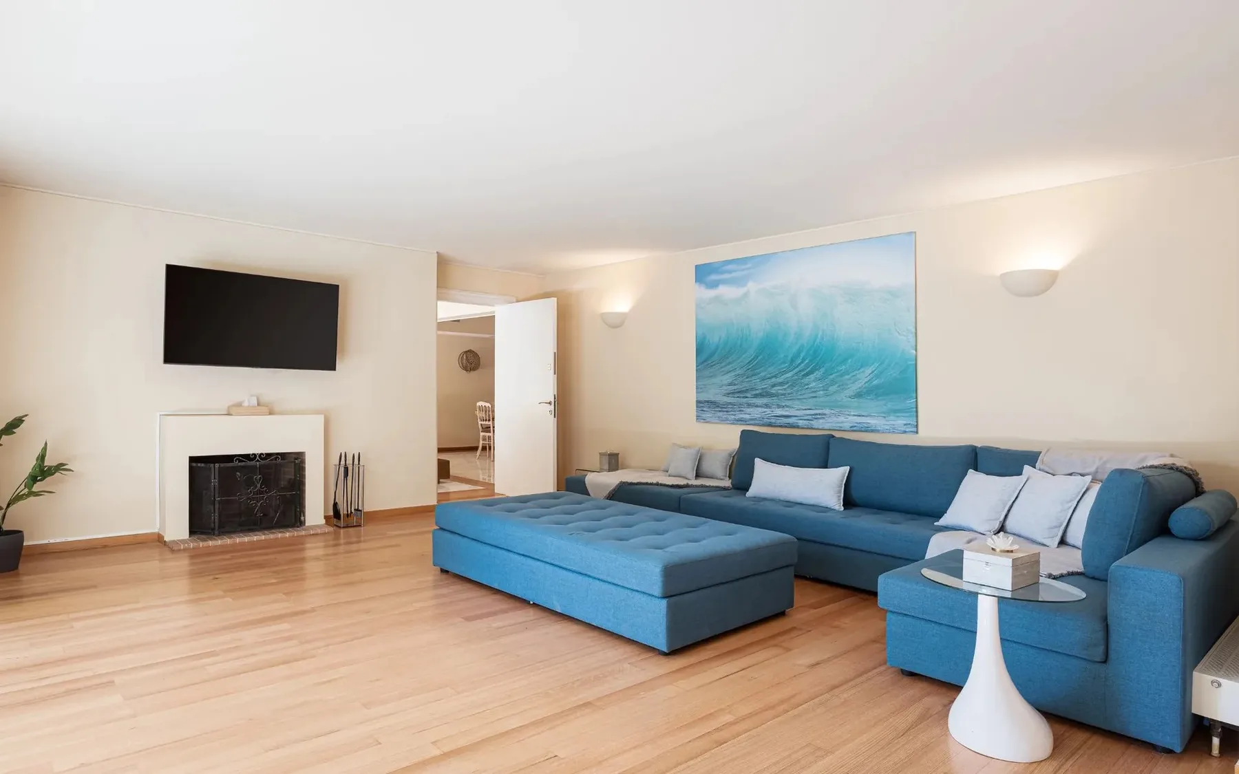 A bright living room with blue seating and a large ocean-wave picture.