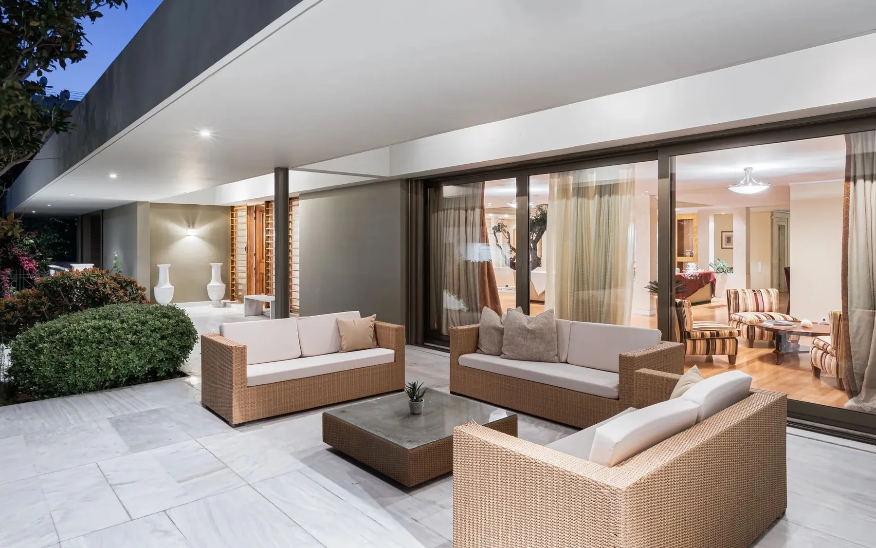An outdoor patio with wicker seating and a low table beside glass doors.