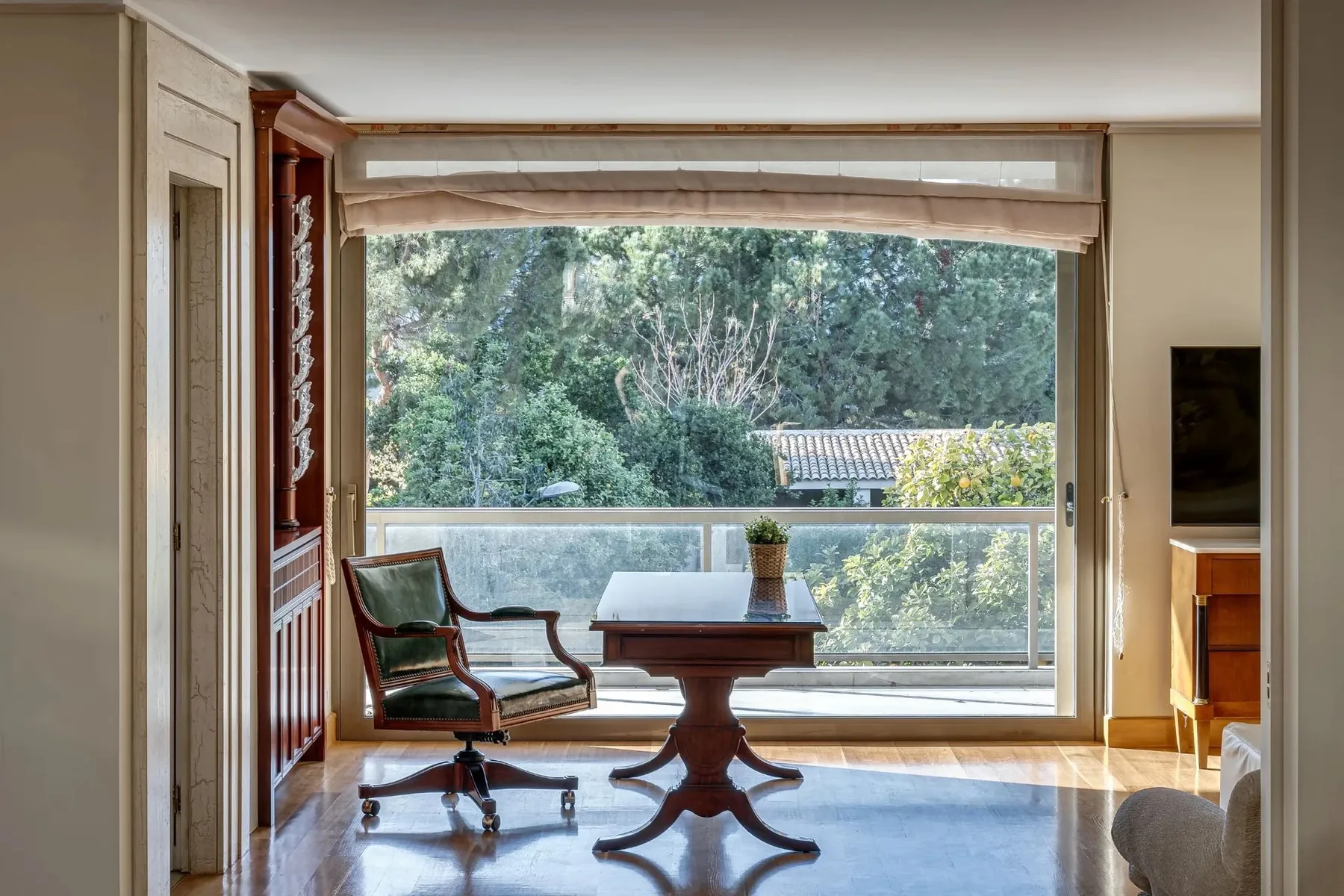 A sitting area faces a large window overlooking green trees.