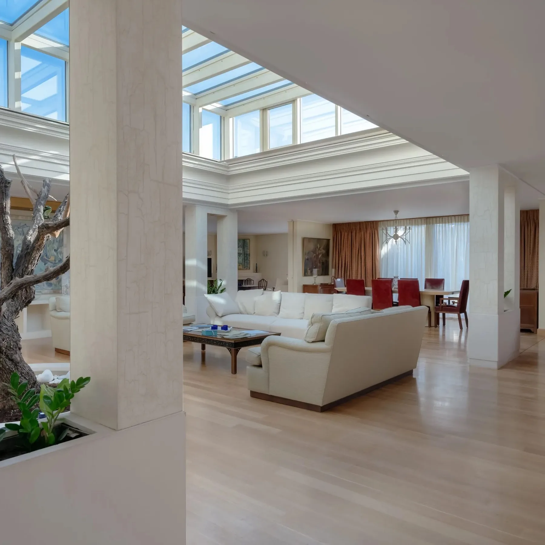A bright living room with white seating beneath a glass ceiling.