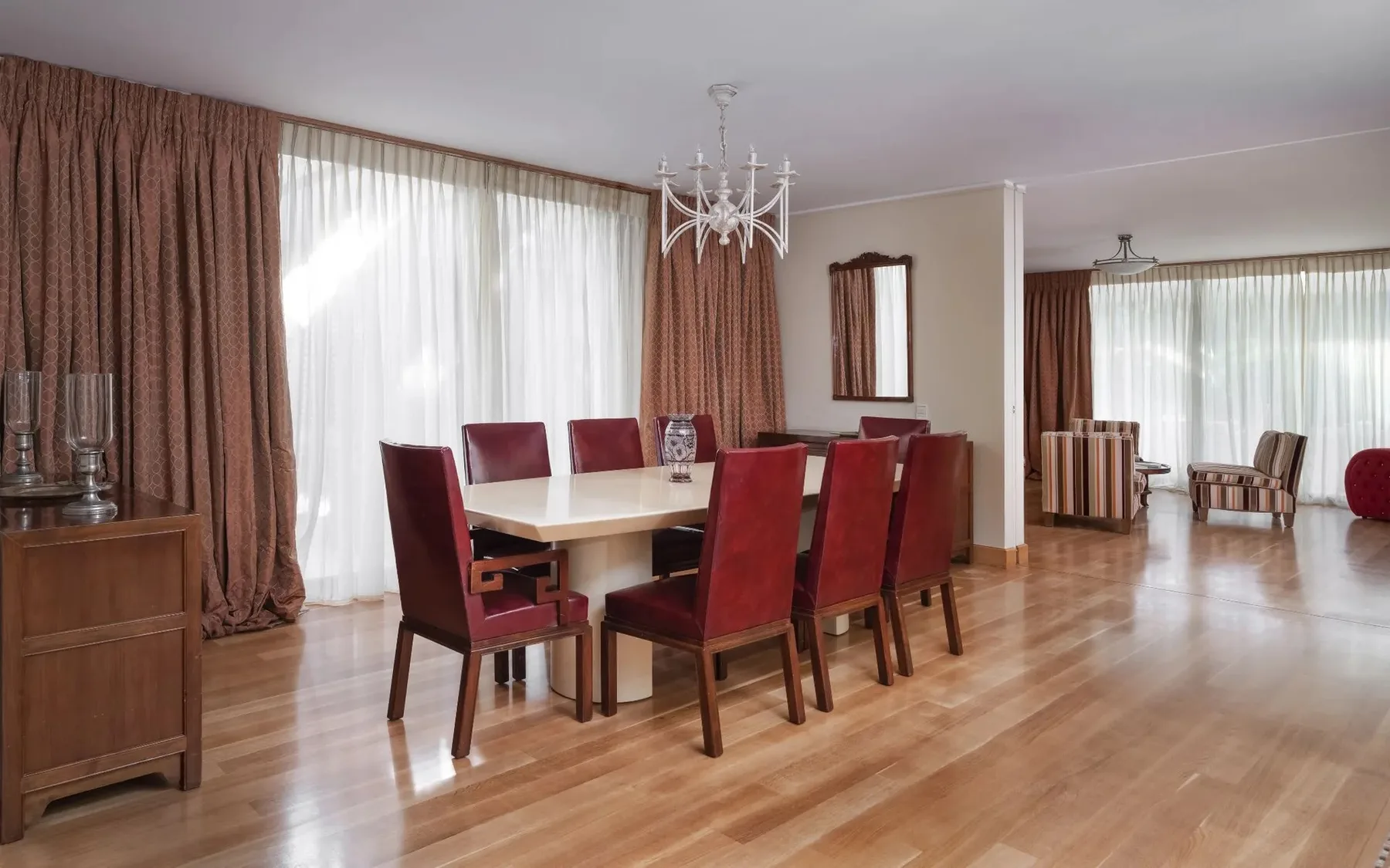 A dining area with a table and red seating beside large curtained windows.