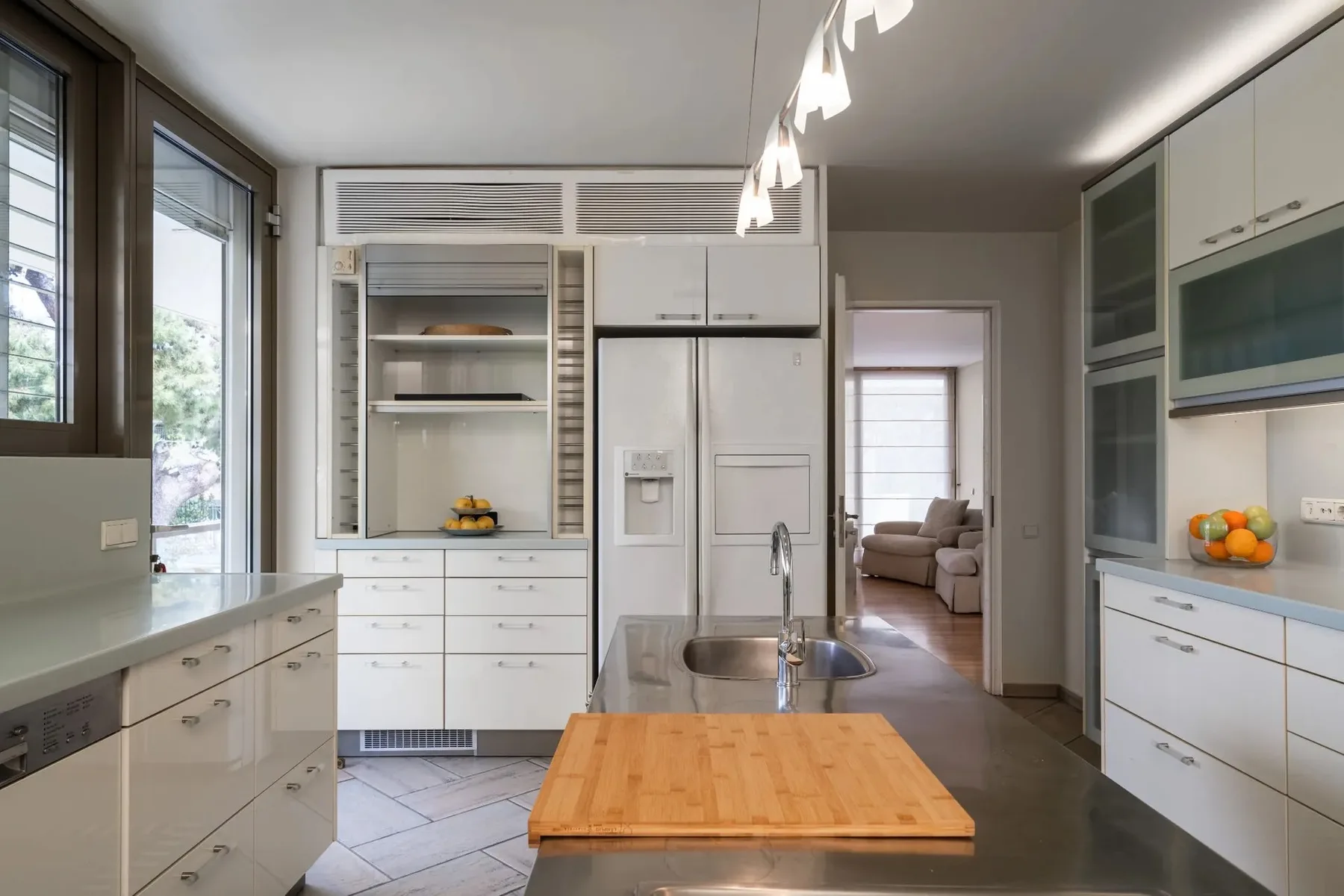 A modern kitchen with white cabinetry, a central island, and large windows.