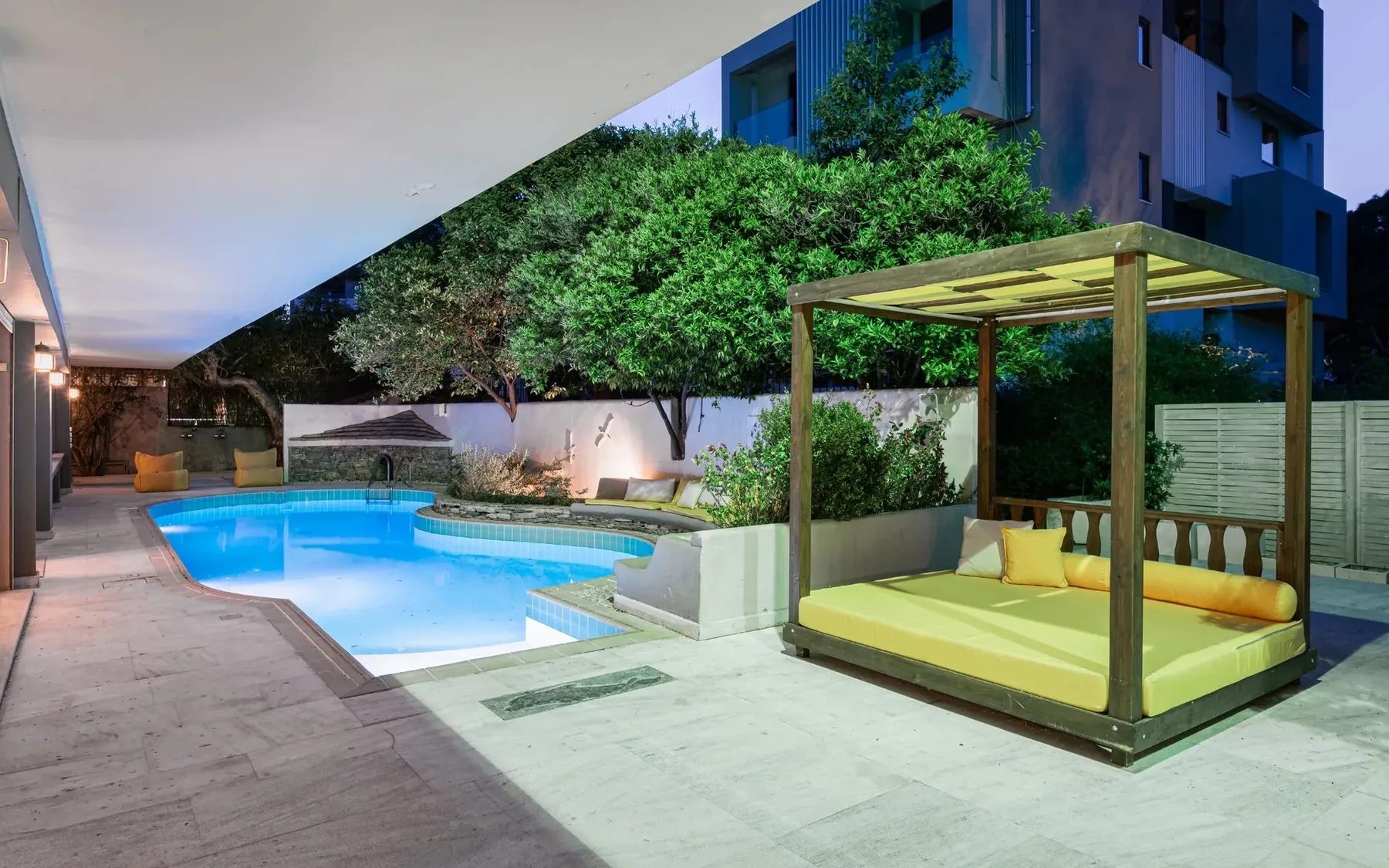 An outdoor pool beside a shaded daybed and landscaped greenery.