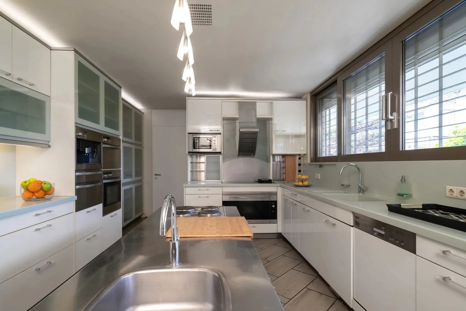 A modern kitchen with white cabinets, a central island, and large windows.
