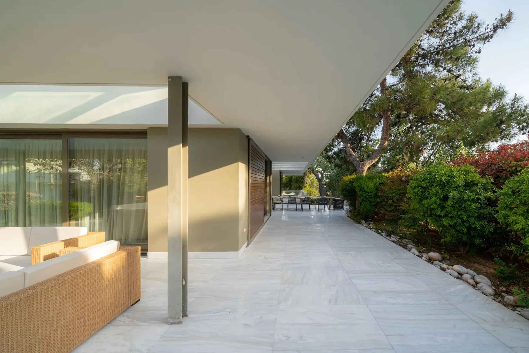A covered patio walkway beside a modern building, with outdoor seating and garden greenery.