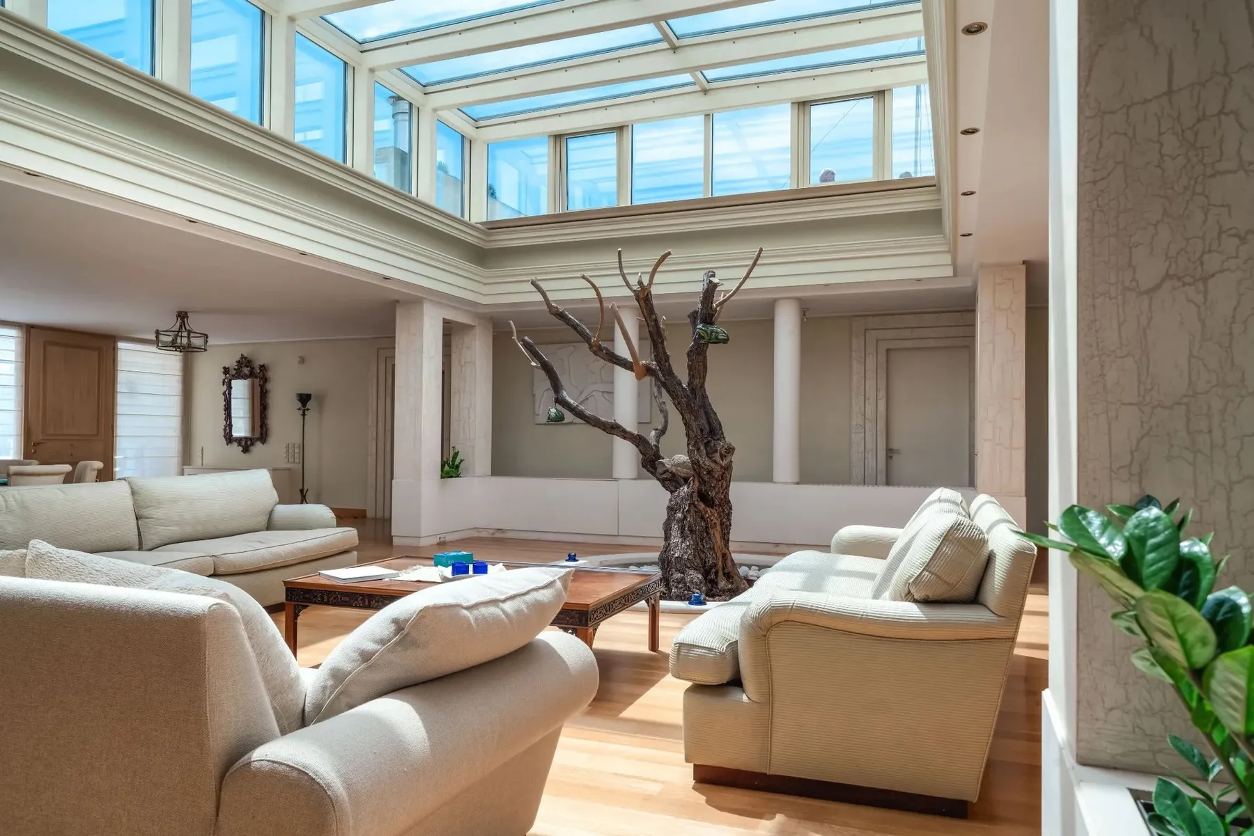 A bright living room with pale seating beneath a large skylight.