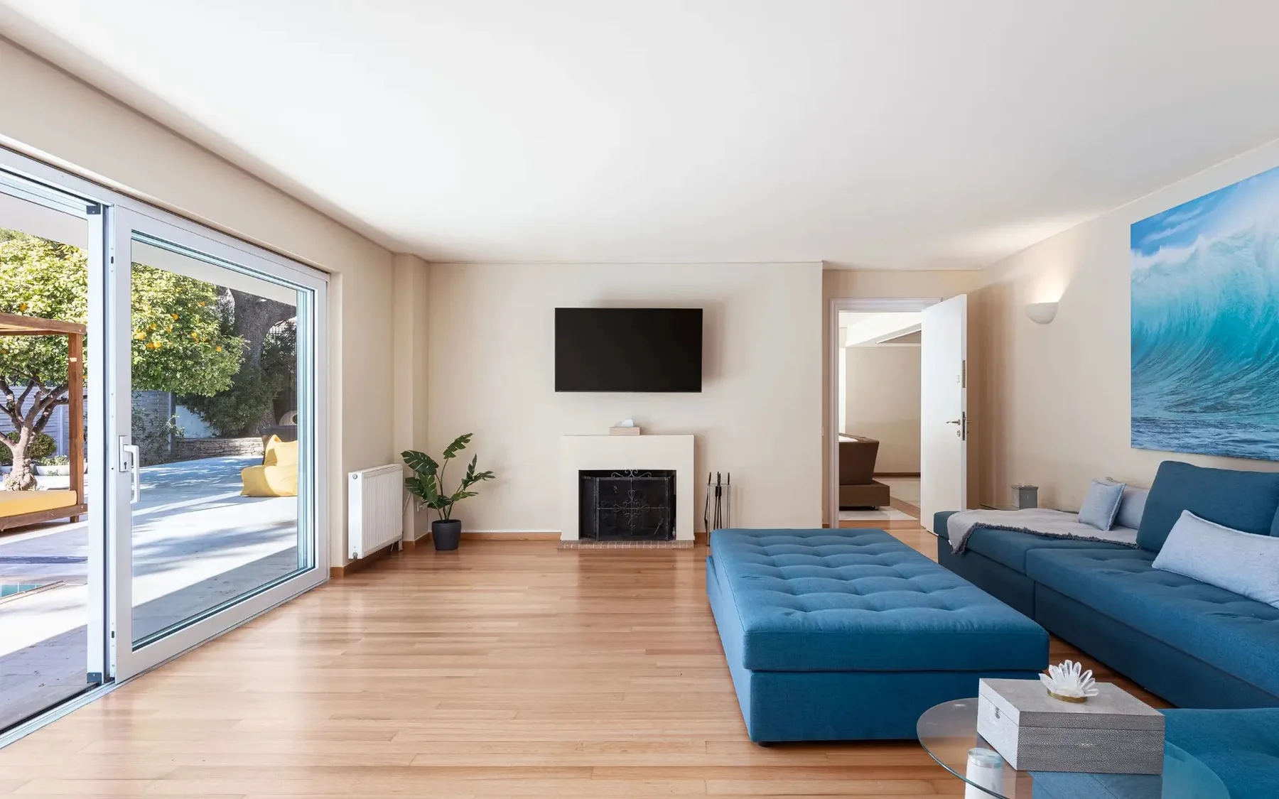 A bright living room with blue seating, a wall-mounted television, and large glass doors.