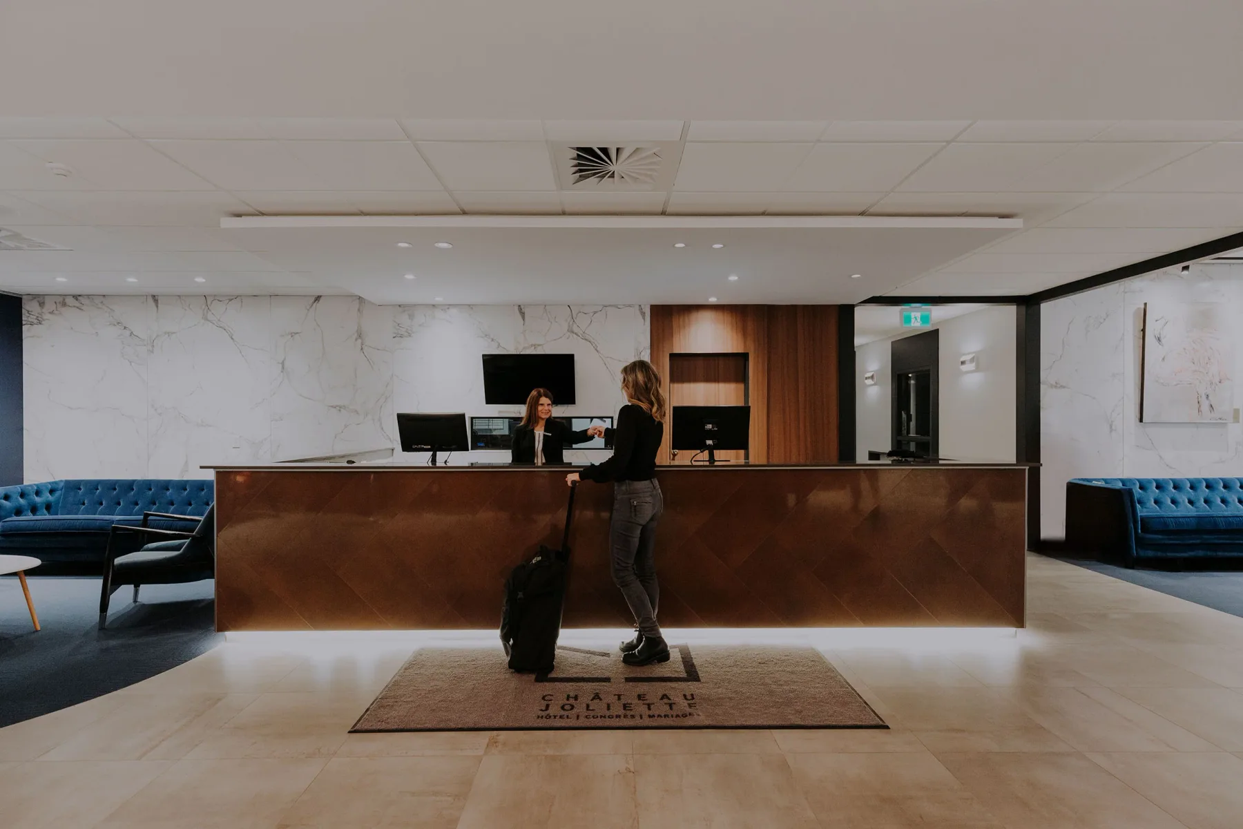 Espacio representativo del hotel: Mostrador de recepción de hotel con una huésped junto a una maleta con ruedas.