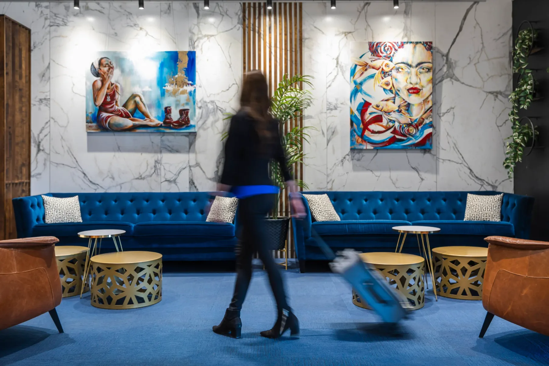 Espacio representativo del hotel: Sala de hotel con asientos azules, mesas redondas y arte colorido en las paredes.