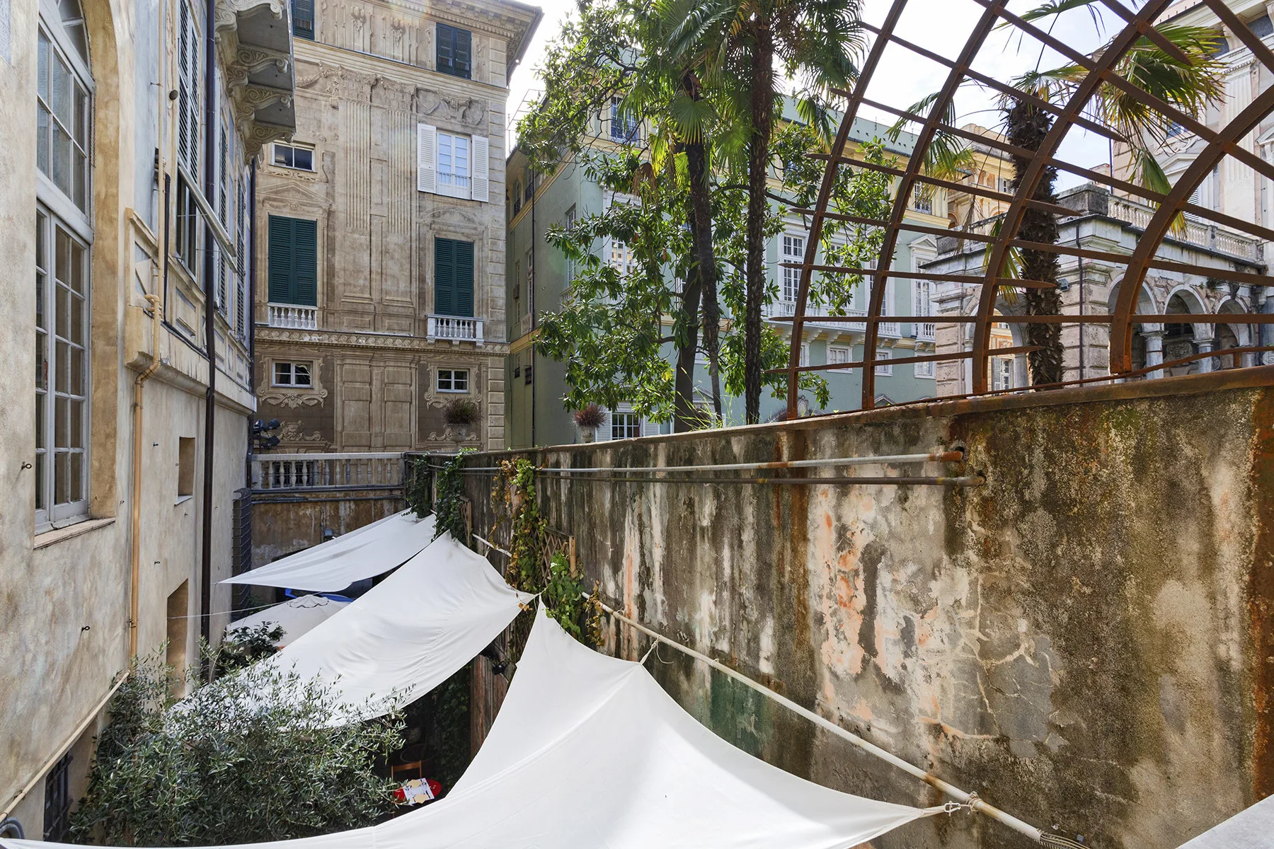Un patio con toldos blancos, edificios alrededor y una estructura metálica curva.