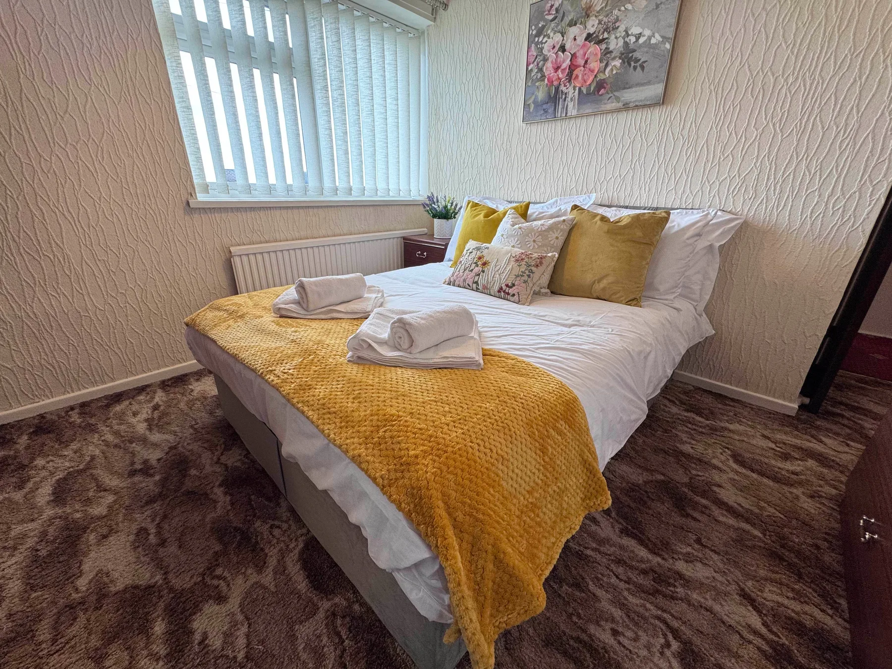 A bedroom with white bedding and a mustard-yellow throw on the bed.