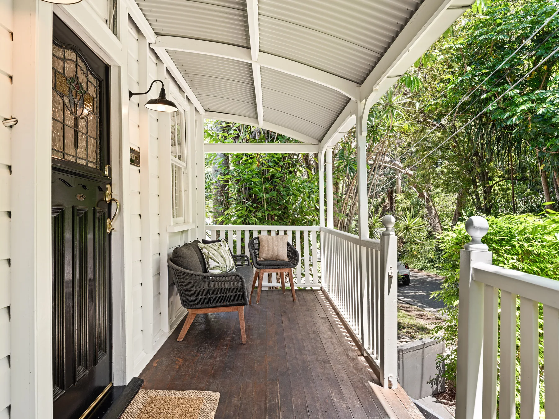 A covered porch with dark seating, white railings, and lush greenery beyond.