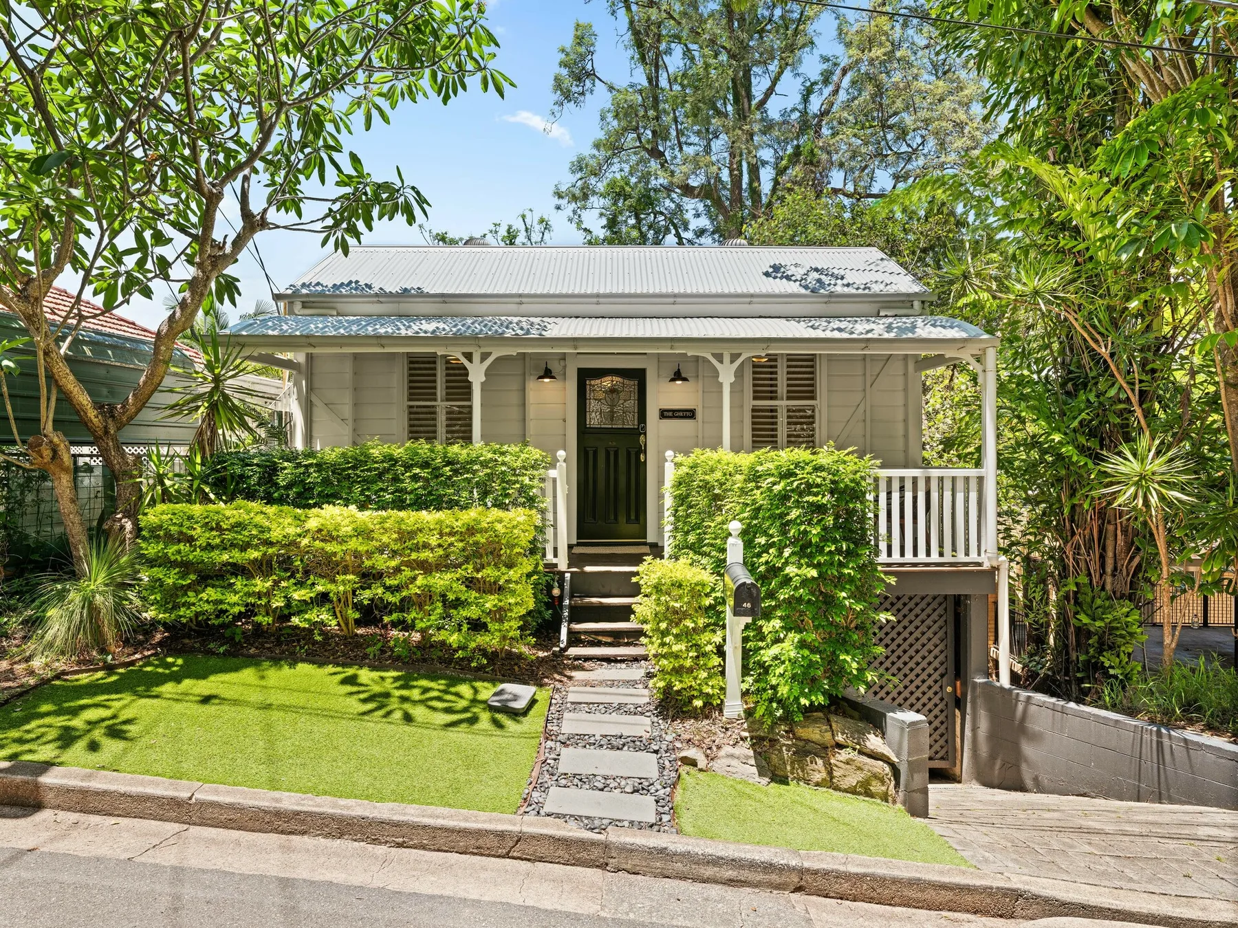 A small house sits behind a garden with trimmed hedges and a stone path.