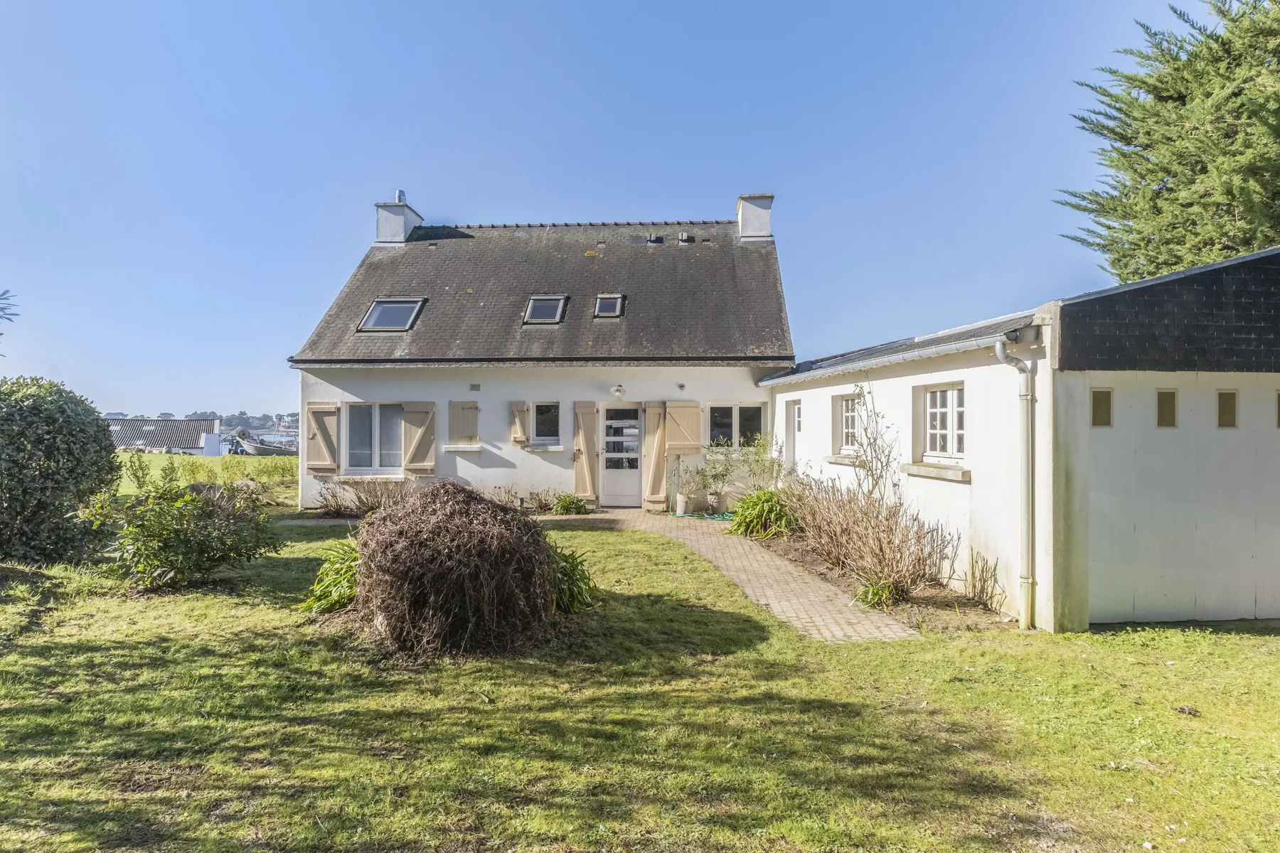 A house and attached outbuilding stand beside a grassy yard and garden path.