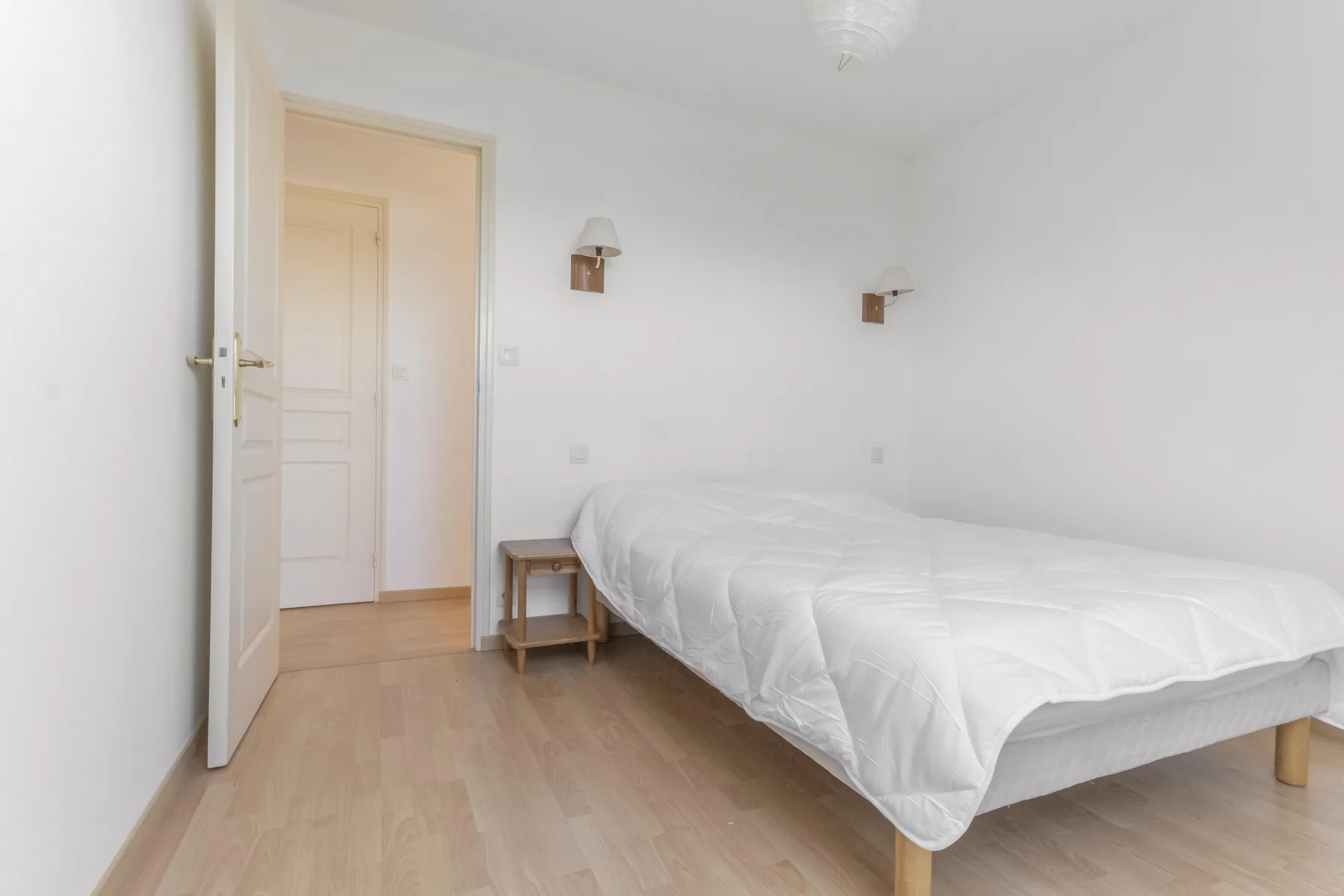 A bedroom with a white bed, bedside table, and open doorway.