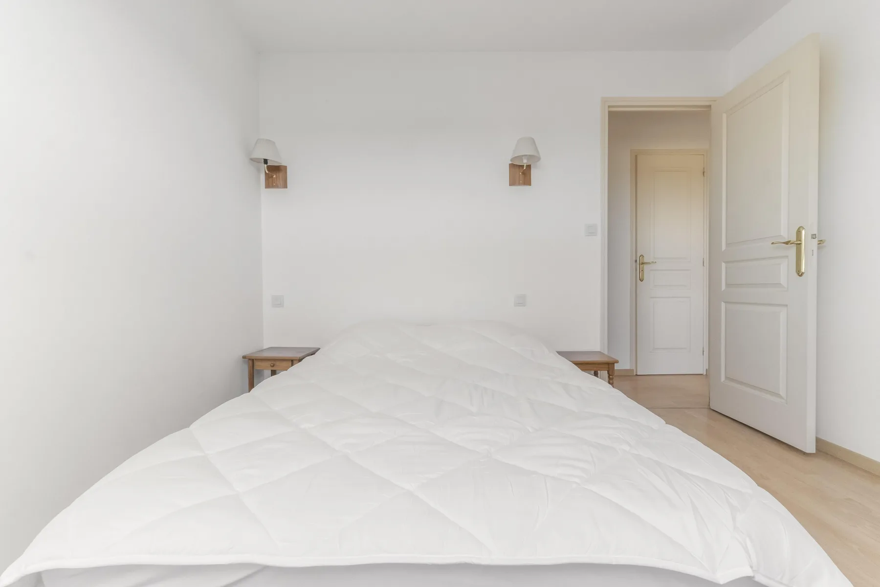 A bright bedroom with a bed, bedside tables, and an open doorway.