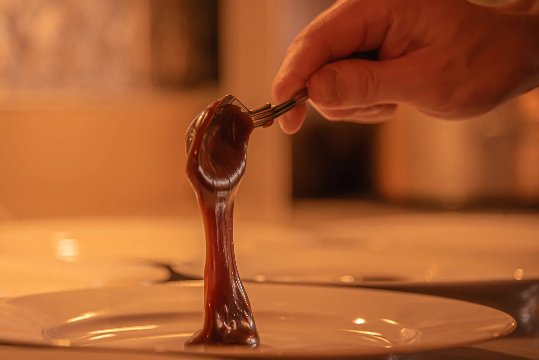 Representative hotel space: A hand lifts a spoonful of melted chocolate over a plate.