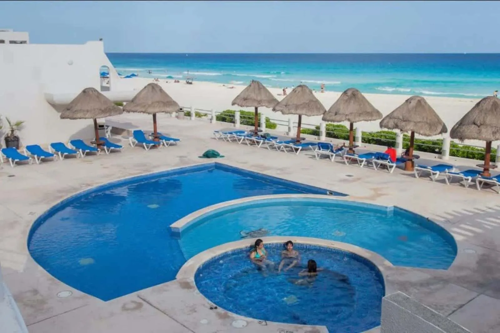 Shared amenity: A swimming pool beside a beach, with lounge seating and thatched shade umbrellas.