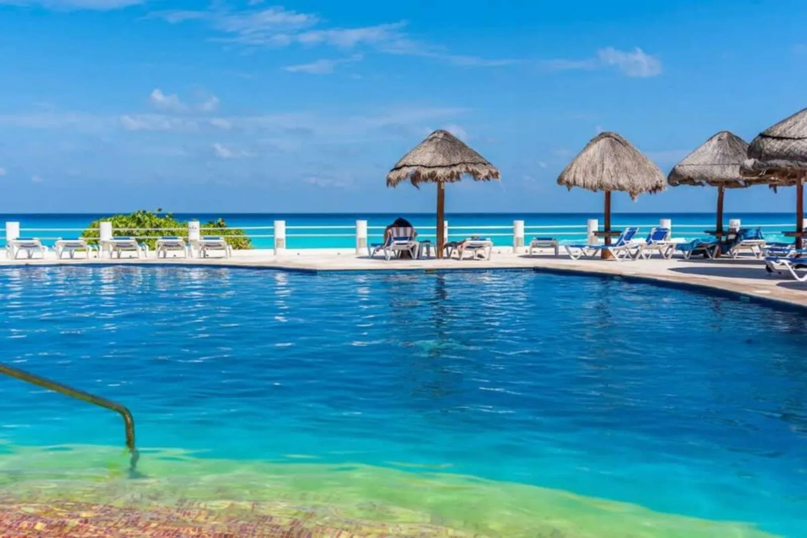 Shared amenity: A swimming pool overlooks the ocean, with lounge seating and thatched parasols along the deck.