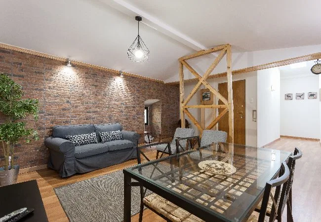 Una sala de estar y comedor tiene un sofá junto a una mesa con tapa de vidrio.