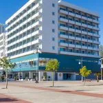 Representative hotel space: A modern multi-story building stands at a street corner beside a broad paved area.