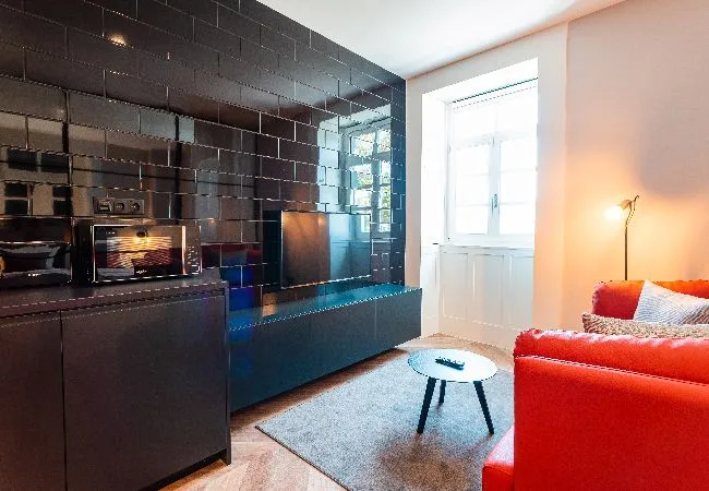 Una sala de estar con una chimenea de azulejos negros, una mesa pequeña y asientos rojos.