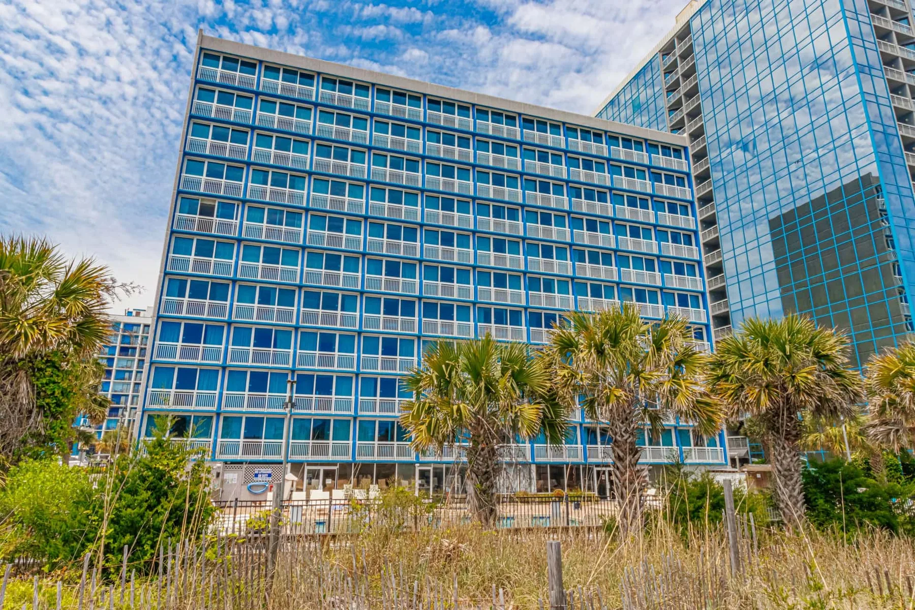 Shared amenity: A large glass-fronted building rises behind palm trees and coastal grasses.