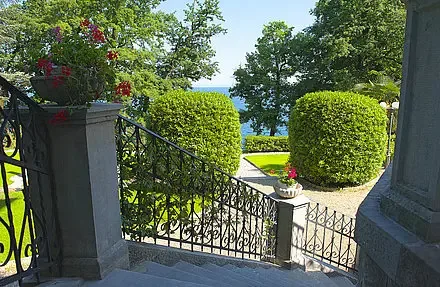 Representative hotel space: A garden walkway with a wrought-iron gate opens toward a lake.