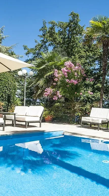Representative hotel space: An outdoor swimming pool is surrounded by lounge seating and flowering plants.