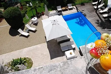 Representative hotel space: A swimming pool beside a paved patio with seating and a large umbrella.