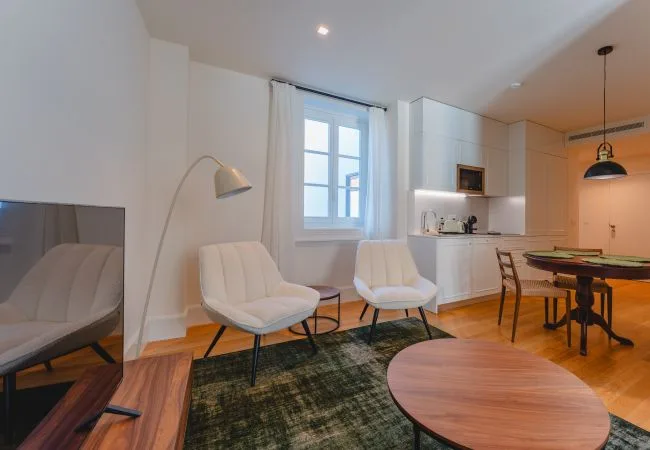 Una luminosa sala de estar y comedor con asientos, una mesa de centro y una cocina compacta.