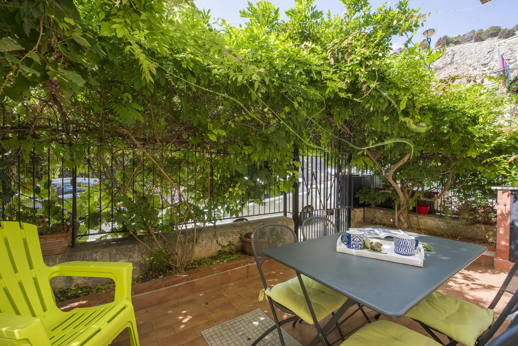 A leafy outdoor patio with a table and chairs beneath a vine-covered pergola.