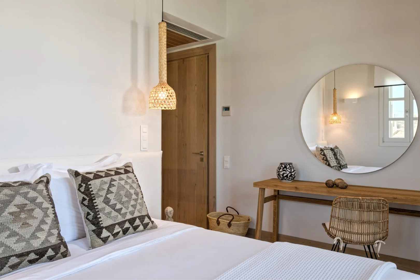 A bedroom with a neatly made bed and a wooden desk beneath a round mirror.