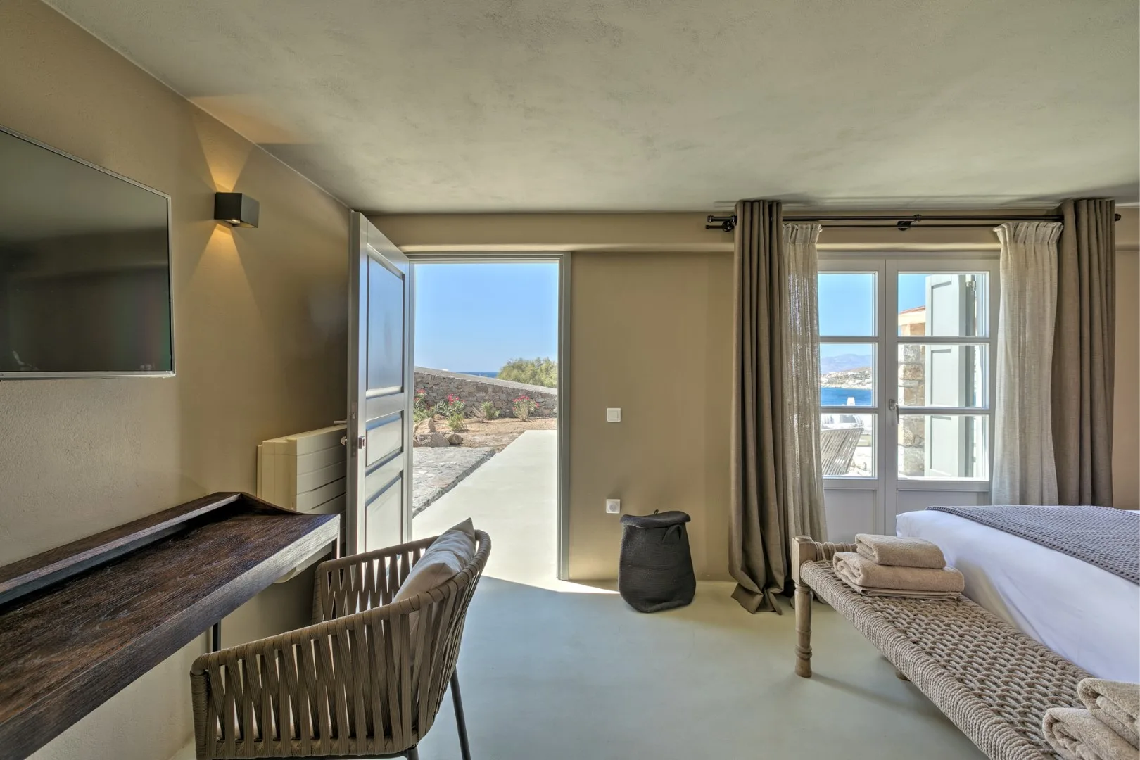A bedroom with a bed beside a large window and an open door to a patio.