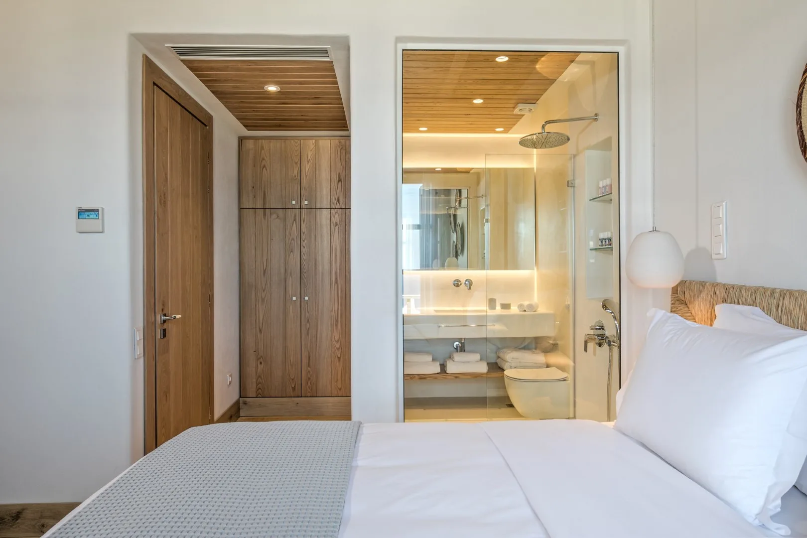 A bedroom with a bed beside a bathroom visible through a glass partition.
