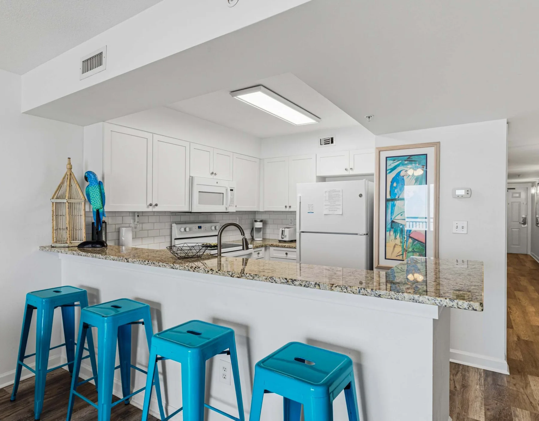 Una cocina luminosa con una barra larga, taburetes turquesa y gabinetes blancos.