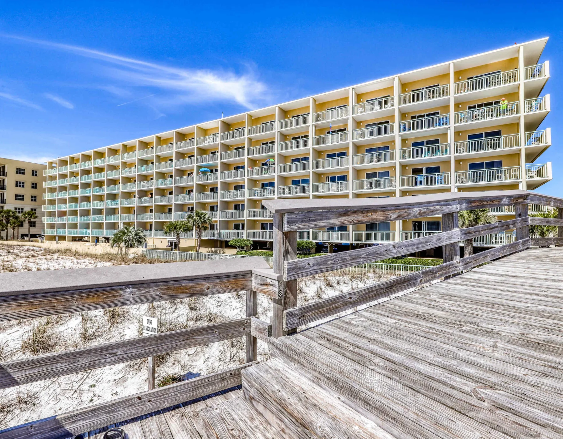 Zona común: Una pasarela con barandillas de madera conduce hacia un edificio de apartamentos junto a la playa.