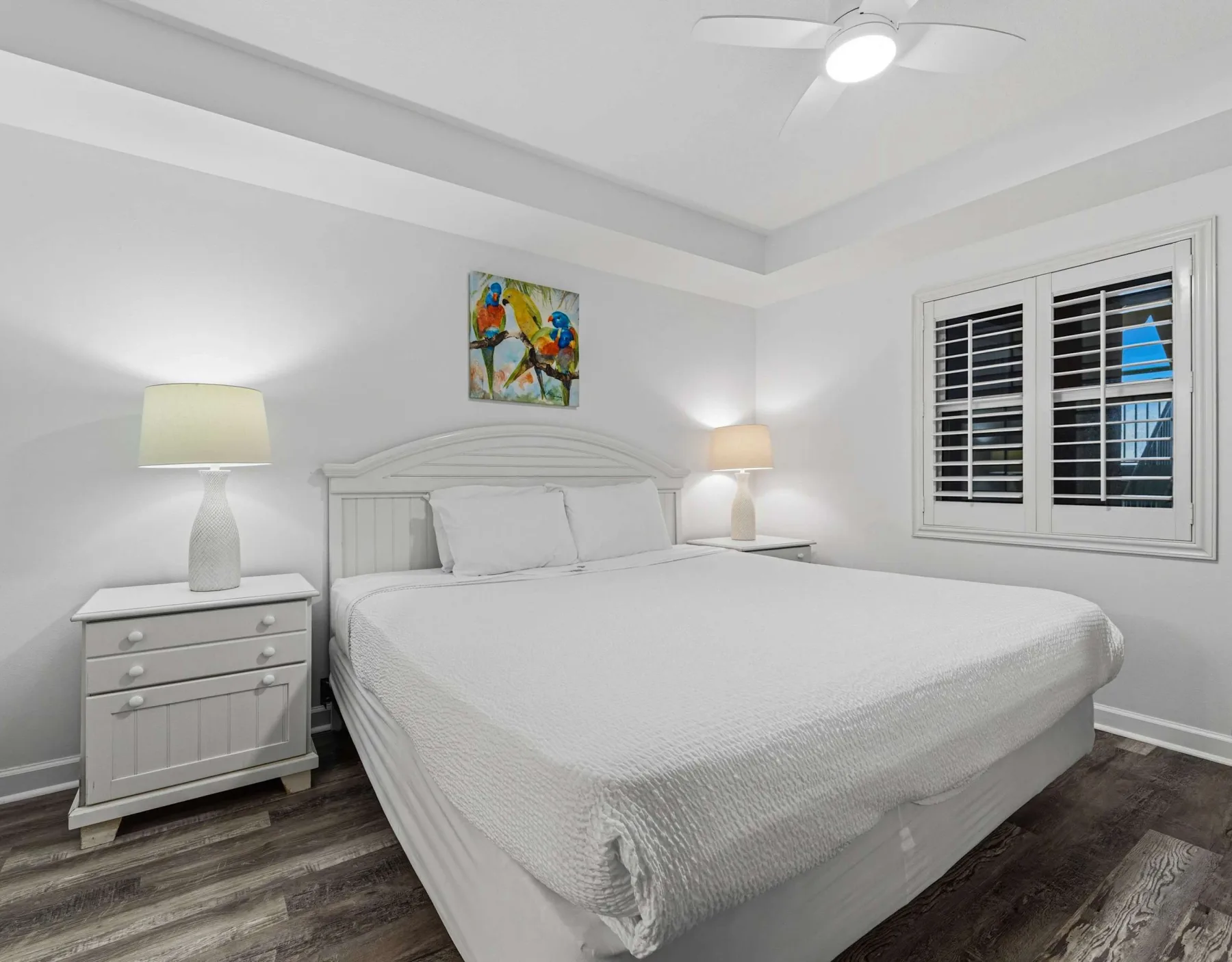 Un dormitorio luminoso con una cama grande, mesitas de noche y una ventana con contraventanas.