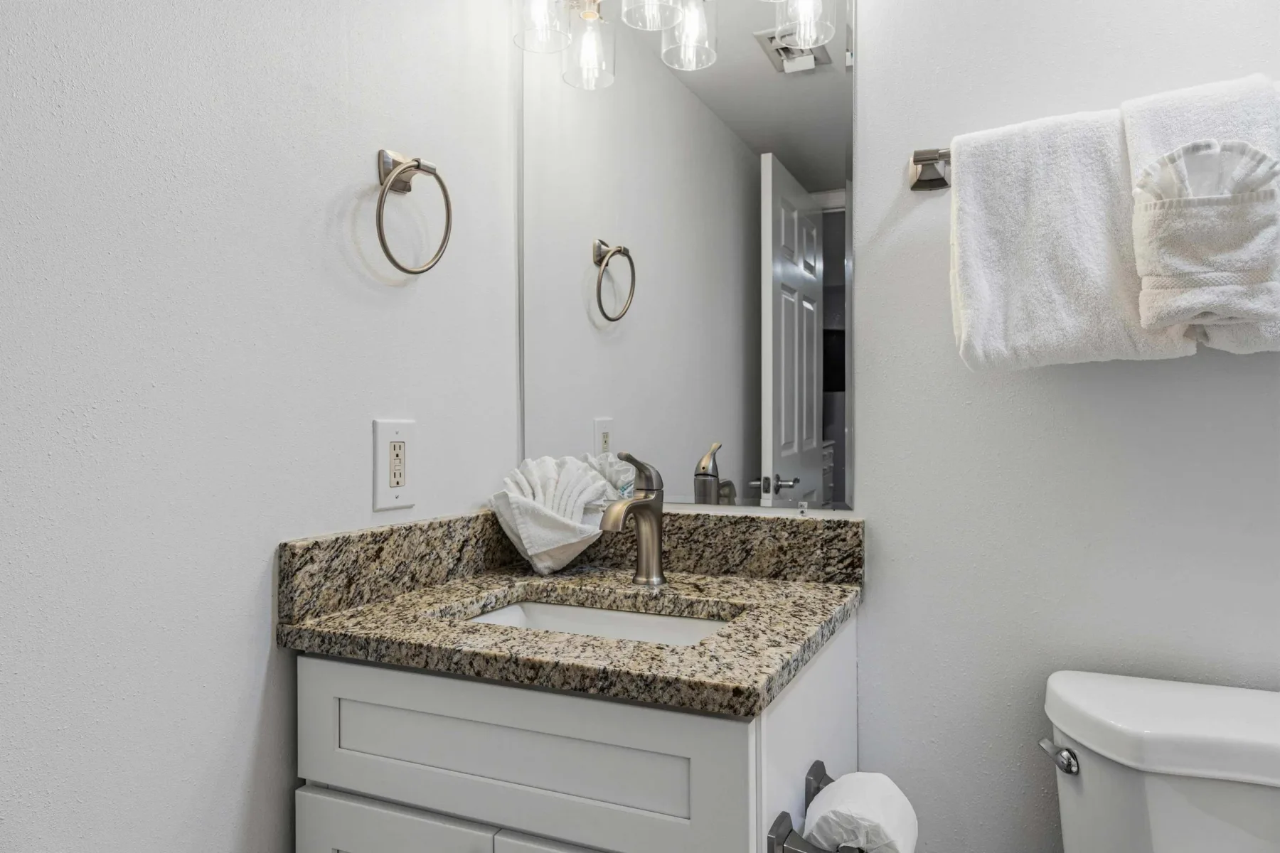 Un tocador de baño con encimera de granito, espejo y toallero.